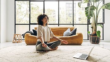 Eine Frau sitzt auf dem Teppich und beginnt mit einer Entspannungstechnik für die Verdauung