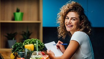 Eine Frau sitzt am Tisch und studiert die Einkaufsliste für eine ausgewogene Ernährung