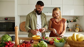 Eine junge Frau und ein junger Mann stehen in der Küche und schneiden Gemüse für eine Low-Fodmap-Ernährung