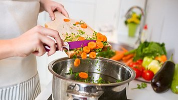 Eine Frau schneidet Gemüse in den Kochtopf für eine gesunde Ernährung