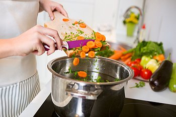 Eine Frau schneidet Gemüse in den Kochtopf für eine gesunde Ernährung